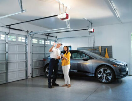 This is a picture of a garage door technician pointing to a garage door opener inside a homeowner's home.