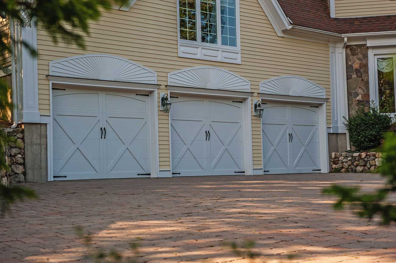 This is an image of white garage doors in a barn carriage house style with handles and straps on a yellow home.