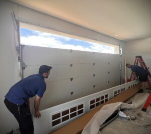Shows garage door installers getting ready to install the final section of the garage door with windows.