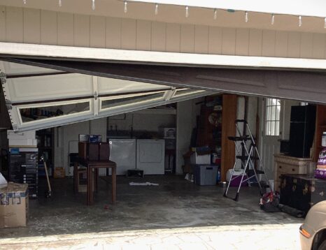 Image of crooked garage door hanging after cables have come off.