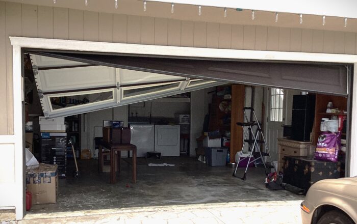 Image of crooked garage door hanging after cables have come off.