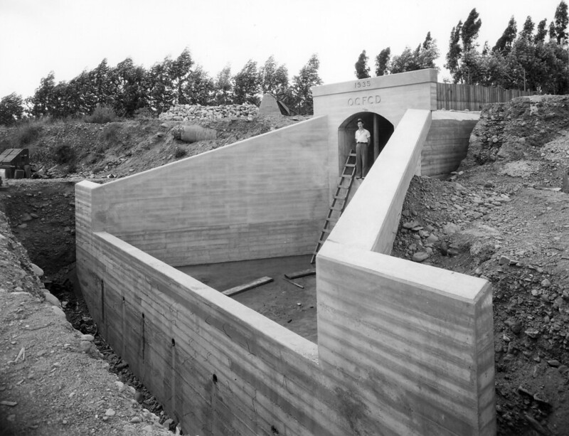 Storm drain building - black and white photo with man standing above ladder.