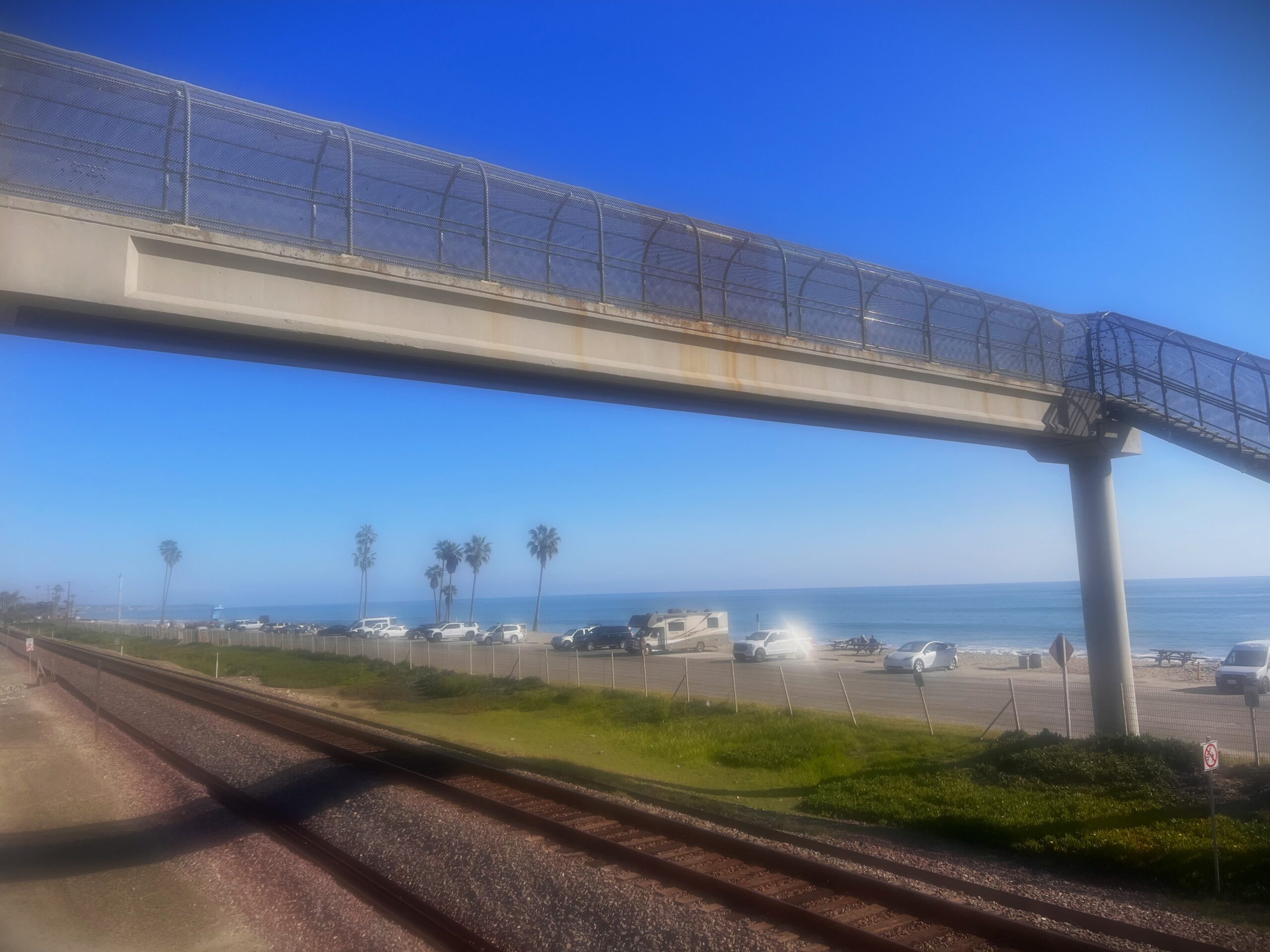 Hole in the fence beach in Capistrano Beach with fence and palm trees.