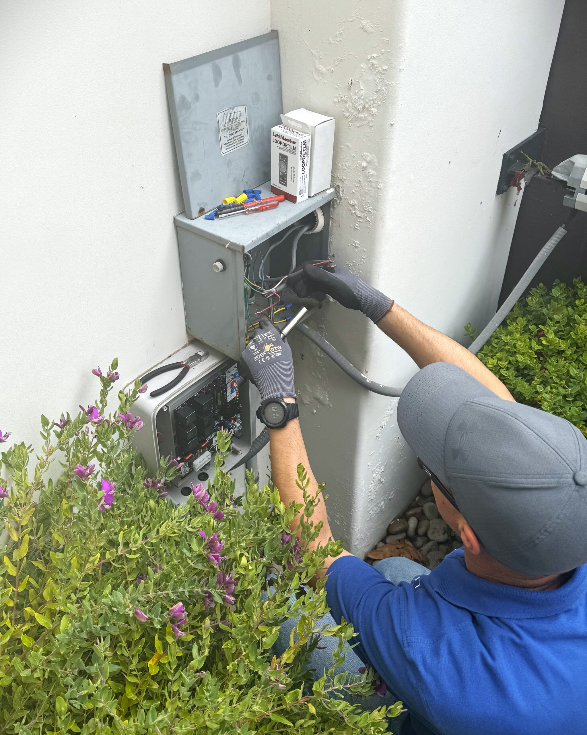 Gate technician working on wiring and circuit board for homeowner's driveway electric gate in Irvine, CA.