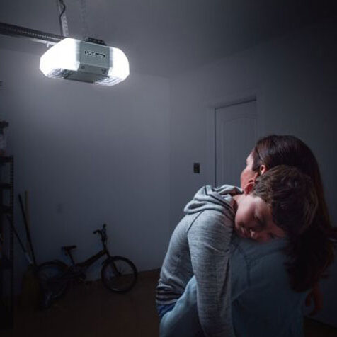Image of a woman in a dark garage looking at her lit up garage door opener that needs repair.